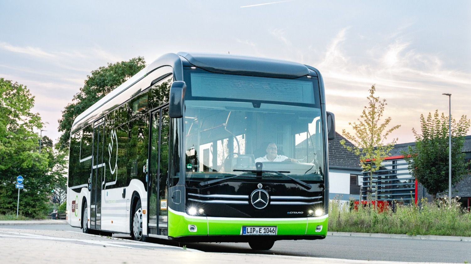 Lippischer Elektro-Stadtbus in Grün-Schwarz-Weiß mit Fahrer am Steuer auf der Straße vor Bäumen und Häusern