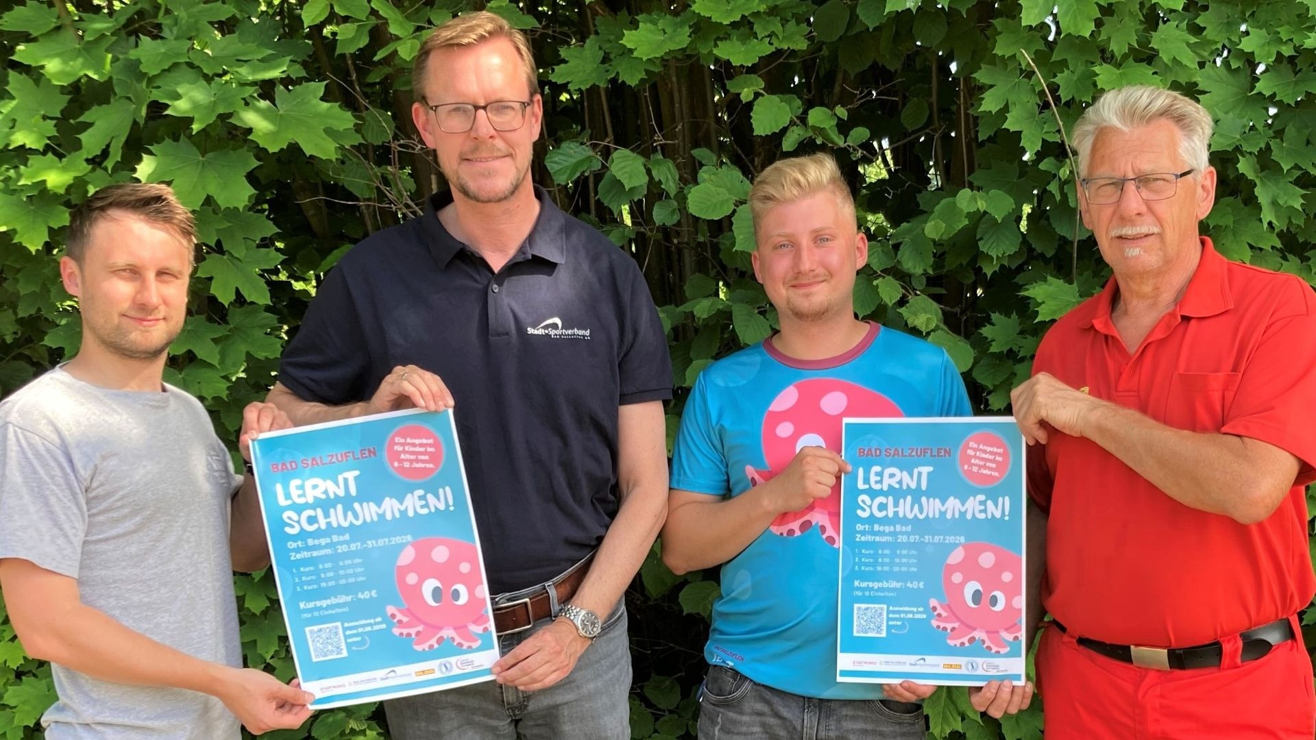 Vier Männer halten zwei blaue Poster mit einem rosa Oktopus und dem Text "Bad Salzuflen lernt Schwimmen!
