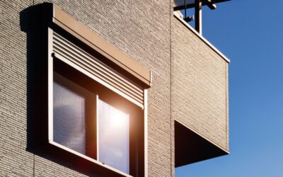 Gebäudefassade mit Fenster und teilweise heruntergelassenem Rollladen unter blauem Himmel im Sonnenlicht