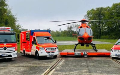 Ein orangefarbener Rettungshubschrauber, ein Intensivtransport-LKW, ein Rettungswagen und ein Notarztfahrzeug auf einer