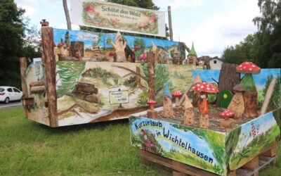 Zwei große Holzdarstellungen einer Wichtel-Miniaturwelt mit Pilzen, Wichtel-Figuren und Umweltschutzbotschaften am
