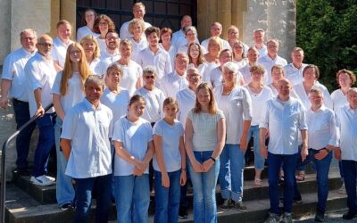 Viele Menschen verschiedenen Alters in weißen Oberteilen und Jeans posieren auf Steinstufen vor einem Steingebäude