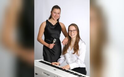 Lina und Julie Holwitt lächeln, Lina mit Mikrofon stehend, Julie am weißen Keyboard spielend