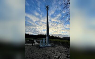 Hoher Mobilfunkmast mit Antennen auf einer Anhöhe unter bewölktem Himmel und Wäldern im Hintergrund