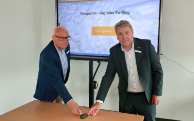 Zwei Männer in Anzügen zeigen auf Computermaus vor Bildschirm mit 'Geoportal - Digitaler Zwilling' und 'Kreis Lippe
