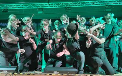Eine Gruppe Asper Schüler mit grünen Blattmasken und schwarzen Kostümen posiert mit ausgestreckten Armen auf einer Bühne