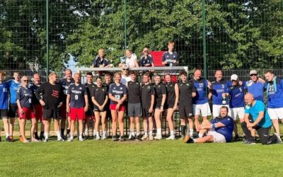Lachende Gruppe Handballer und Handballerinnen posiert mit Pokal auf Sportplatz vor Tor
