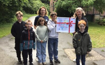 Fünf Kinder und zwei Frauen stehen auf einem Weg, ein Junge und eine Frau halten ein gerahmtes, buntes Bild mit roter