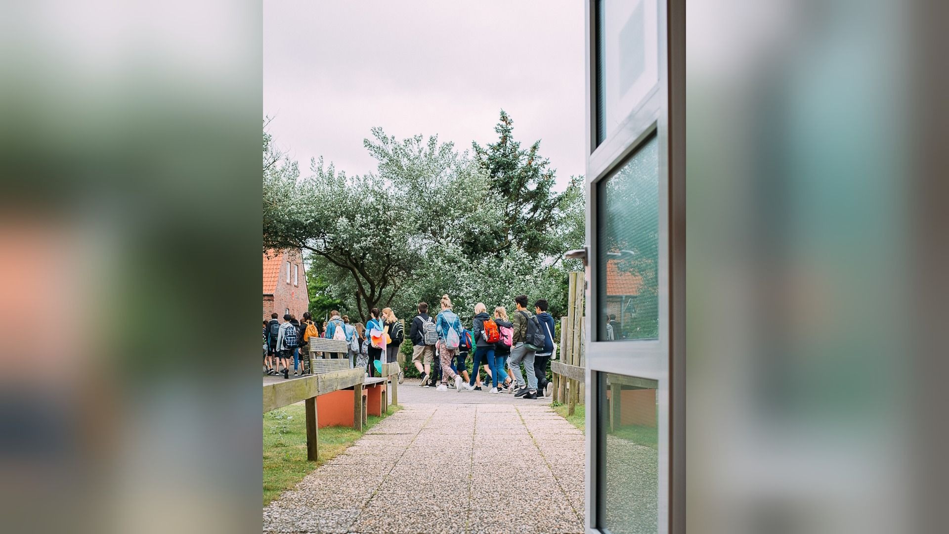 Gruppe junger Leute mit Rucksäcken läuft auf einem gepflasterten Weg zwischen Bäumen zum Haus Detmold