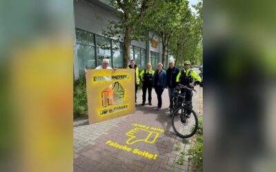 Zwei Polizisten, ein Radfahrer und drei weitere Personen mit Schildern zur sicheren Fahrtrichtung auf einem Weg