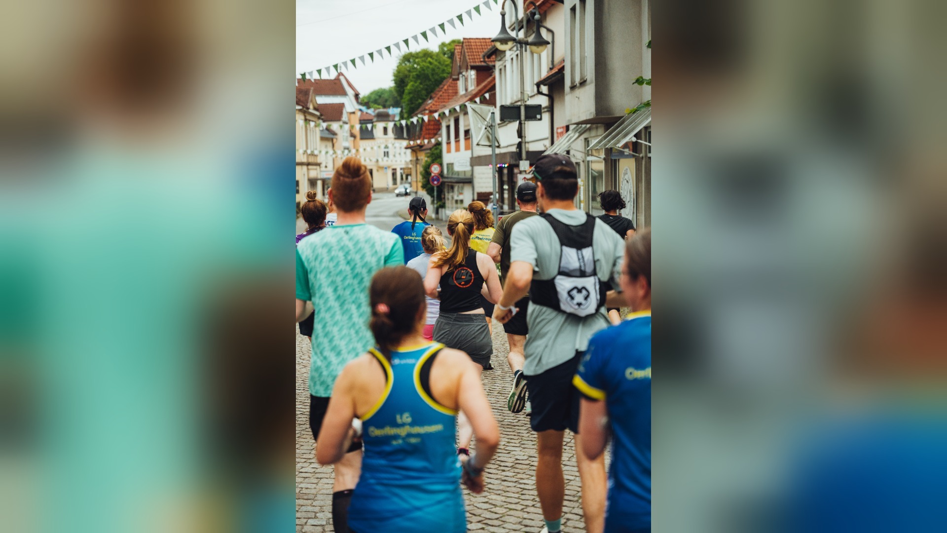 Gruppe Läufer von hinten auf einer gepflasterten Straße mit Häusern und bunten Wimpelketten