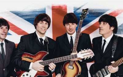 Vier Musiker in dunklen Anzügen mit Gitarren und Mop-Top-Frisuren vor britischer Flagge