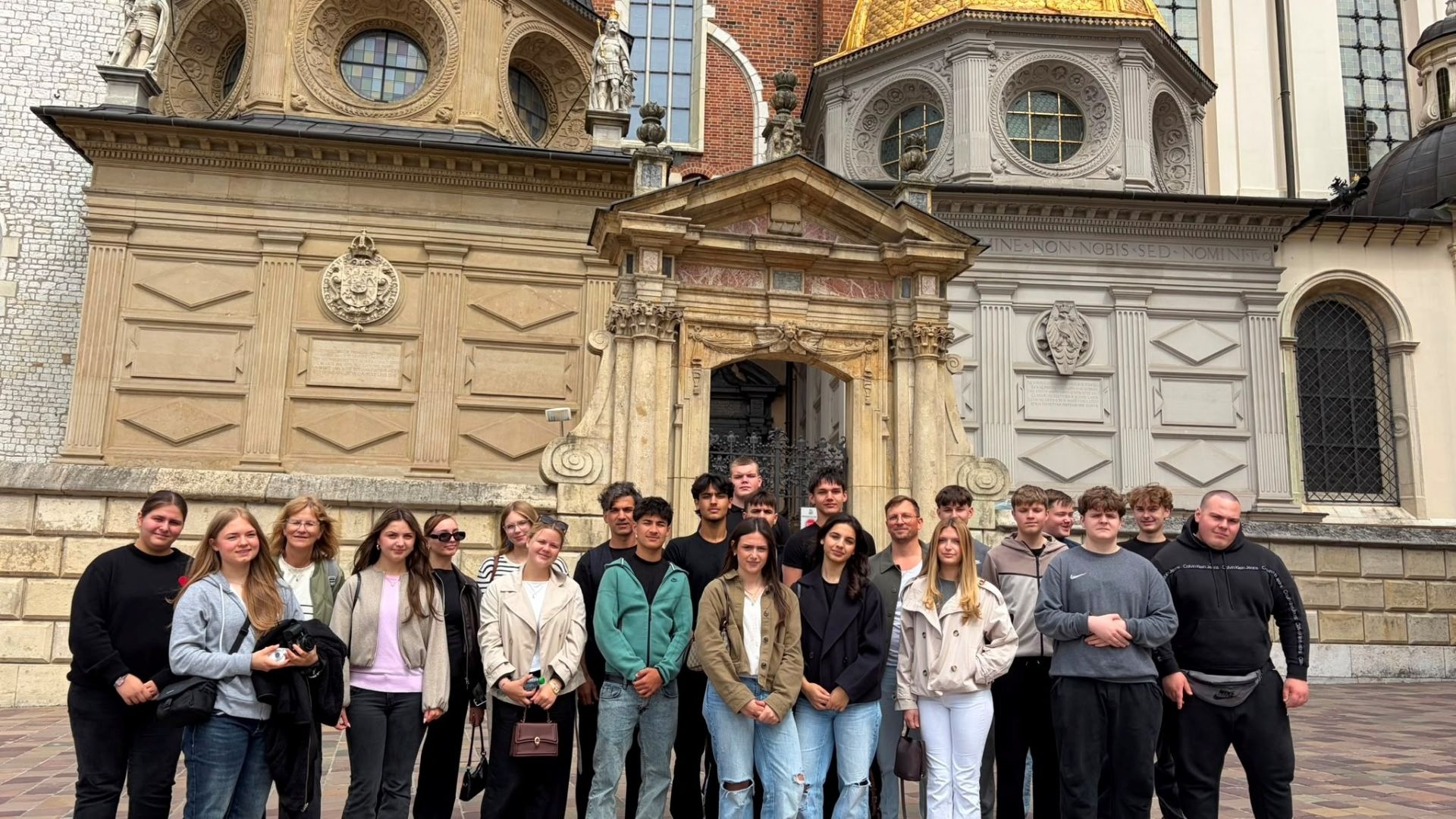 Viele Schüler und Lehrer stehen vor der Fassade einer Kathedrale mit goldenem Dach in Krakau