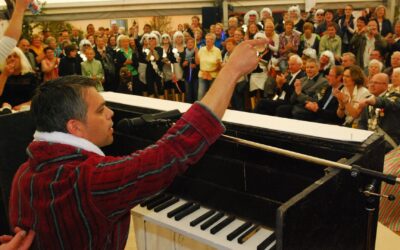 Mann in roter Streifenrobe performt am Klavier und zeigt auf eine begeisterte Zuschauermenge