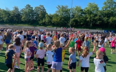 Eine große Gruppe Kinder steht auf einem Sportplatz, viele haben die Arme erhoben