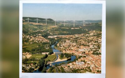 Luftaufnahme der Stadt Millau im Tal mit dem Fluss Tarn und der langen Millau-Brücke über den Hügeln