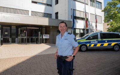 Roxana Keil-Preuß in Polizeiuniform lächelt vor dem Rathaus und einem Polizeiwagen