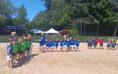 Mehrere Kindergruppen in Sporttrikots stehen mit Erwachsenen auf einem Sandfeld beim Beachhandball