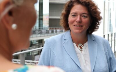 Kerstin Vieregge mit braunem Haar und blauem Blazer lächelt im Gespräch vor moderner Architektur