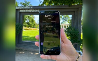 Hand hält Smartphone mit Bad Salzuflen App, die Wetter und SalzuflenCARD anzeigt, vor einem Parkschild