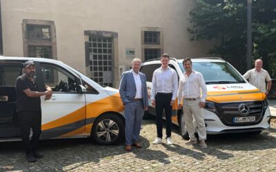 Fünf Männer posieren auf Kopfsteinpflaster vor zwei weißen LIMO-Vans mit orangefarbenen Streifen und dem Gebäude der