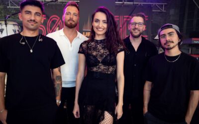 Eine Frau und vier Männer der Band UpTones lächeln auf einer Bühne mit Instrumenten