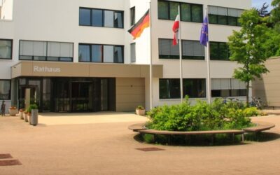 Weißes Rathausgebäude mit "Rathaus"-Schriftzug, deutschen, polnischen und EU-Flaggen, davor ein Platz mit Bänken und