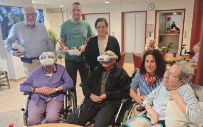 Zwei Senioren tragen VR-Brillen, umgeben von anderen Senioren und Betreuern in einem Aufenthaltsraum