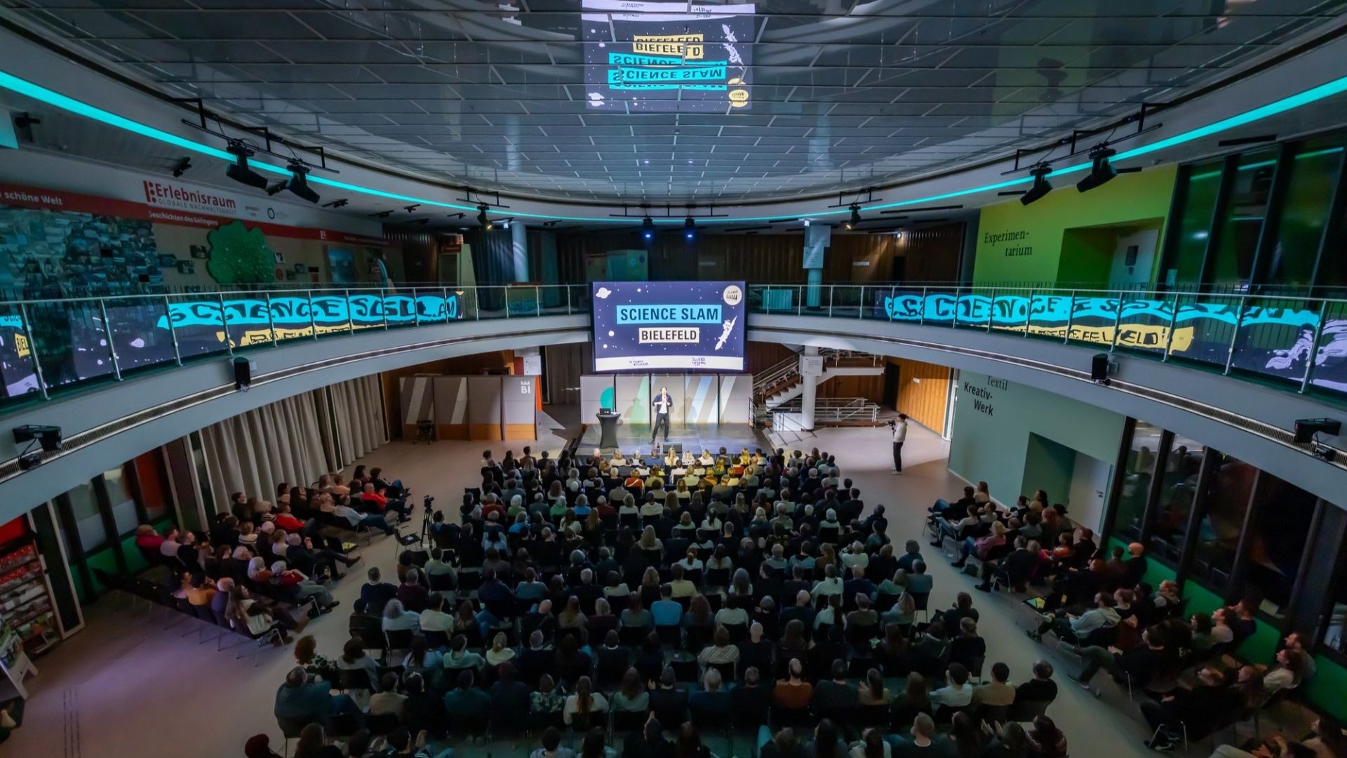 Mann spricht auf Bühne vor großem Publikum beim Science Slam Bielefeld in einem modernen Veranstaltungssaal