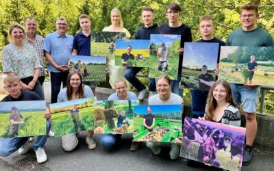 Fünfzehn Personen, viele junge Landwirte, halten draußen vor grünen Bäumen Plakate mit Landwirtschaftsmotiven