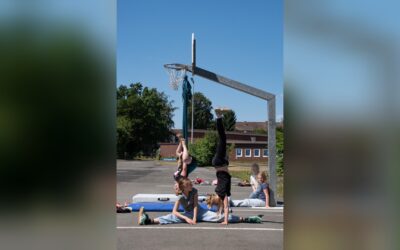 Mädchen machen Handstand, Spagat und hängen kopfüber auf einem asphaltierten Sportplatz vor einem Basketballkorb
