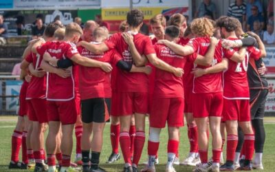 Fussballspieler des TuS Lipperreihe in roten Trikots bilden einen Kreis auf dem grünen Fussballfeld