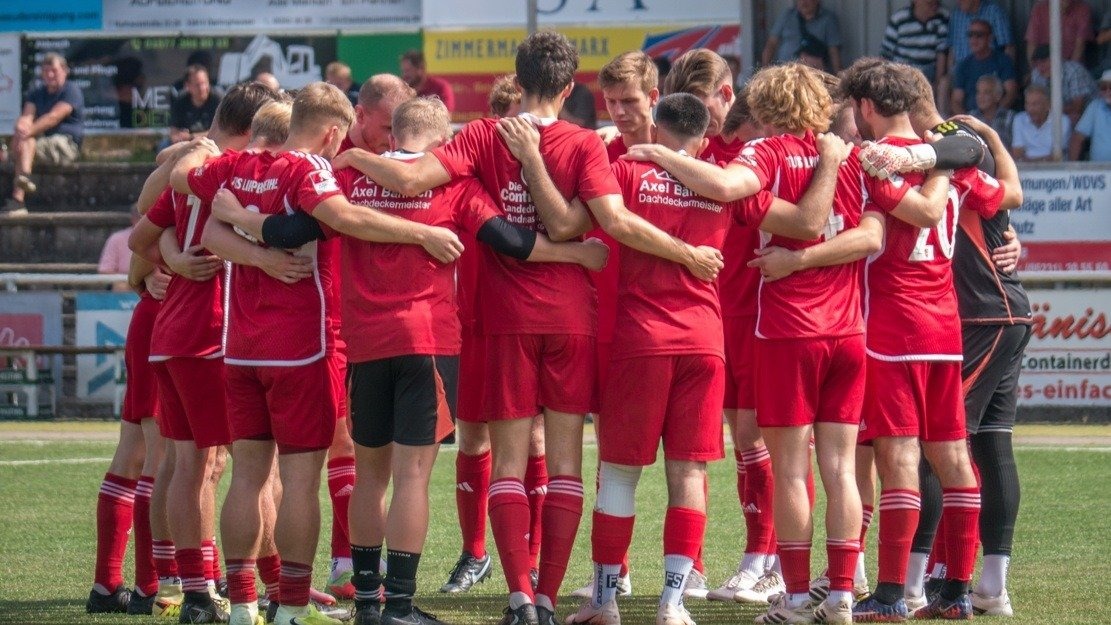 Fussballspieler des TuS Lipperreihe in roten Trikots bilden einen Kreis auf dem grünen Fussballfeld