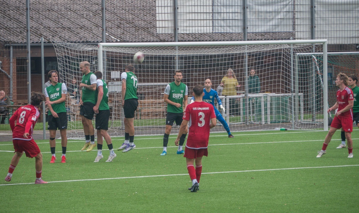 TuS Lipperreihe-Spieler in Rot und Gegner in Grün stehen vor dem Tor, Ball fliegt über springende Spielerwand