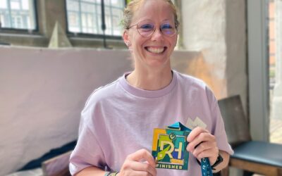 Lächelnde Frau mit Brille hält eine bunte Triathlon-Finisher-Medaille der DATEV Challenge Roth 2022