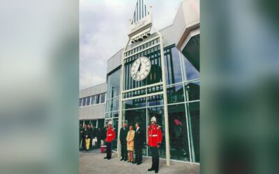Eine große Big-Ben-artige Uhrfassade mit Jaguar-Logo vor einem modernen Gebäude, davor zwei Gardisten und drei Personen