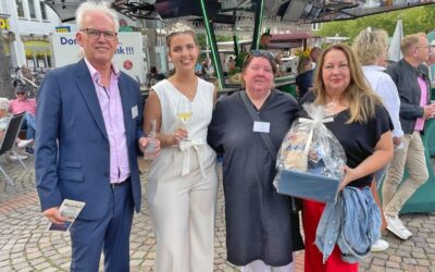 Vier Personen auf einem Weinfest: Ein Mann hält einen Flyer, eine Frau ein Weinglas, eine weitere Frau einen Präsentkorb