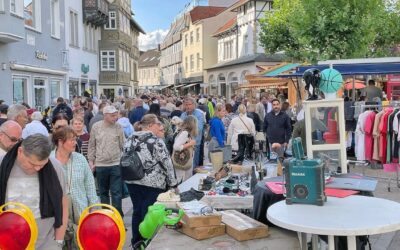 Großer Flohmarkt auf einer Stadtstraße mit vielen Besuchern, die Stände mit Kleidung, Schuhen und Trödel durchstöbern