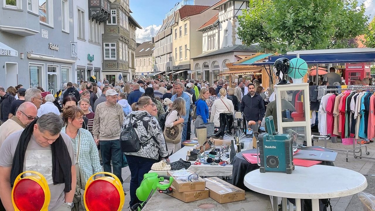 Großer Flohmarkt auf einer Stadtstraße mit vielen Besuchern, die Stände mit Kleidung, Schuhen und Trödel durchstöbern