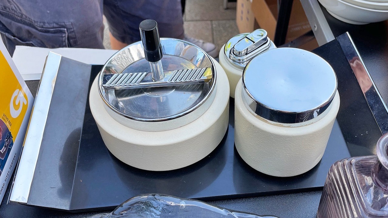 Zwei cremefarbene Aschenbecher mit Chromdeckeln und ein kleines Feuerzeug auf einem Marktstand