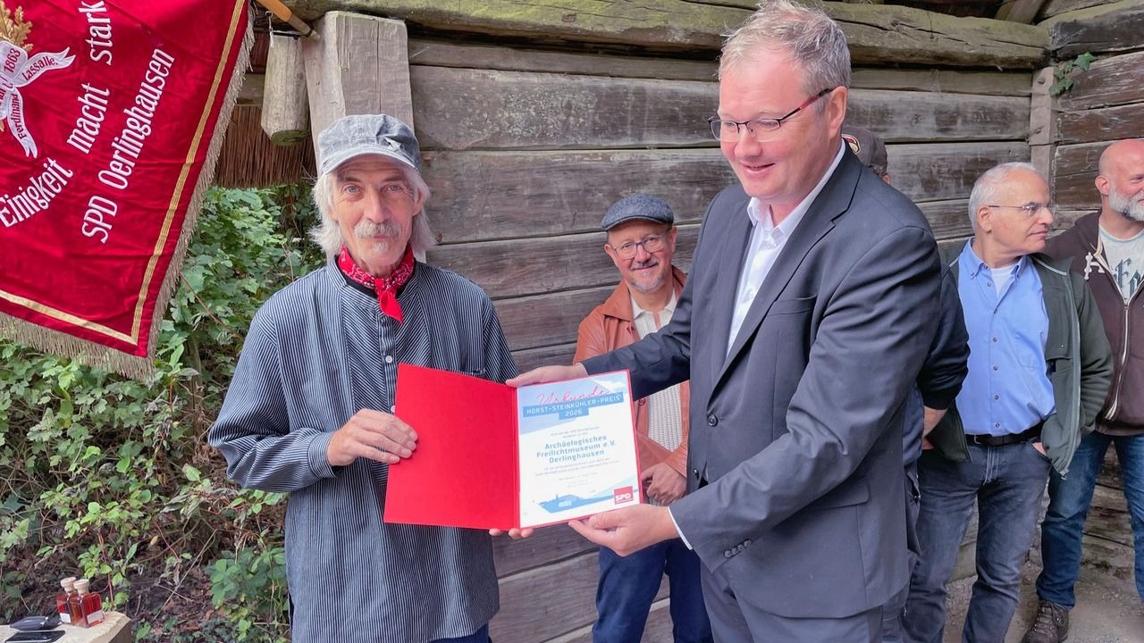 Mann im Anzug übergibt Urkunde des Horst-Steinkühler-Preises an Vertreter des Archäologischen Freilichtmuseums