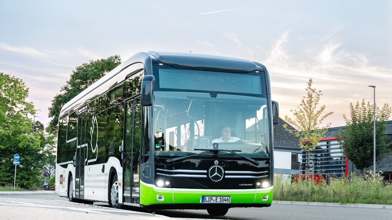 Mercedes-Benz eCitaro Bus in Grün-Schwarz mit lächelndem Fahrer auf einer Straße unter blauem Himmel