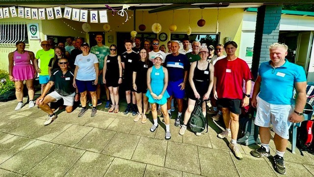 Gruppe von über 20 Personen in Sportkleidung steht vor einem Clubhaus mit Schleifchenturnier-Banner