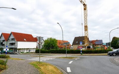 Straßenkreuzung mit modernen Wohngebäuden, einem Baugelände mit Kran, älteren Häusern und einem fahrenden Auto