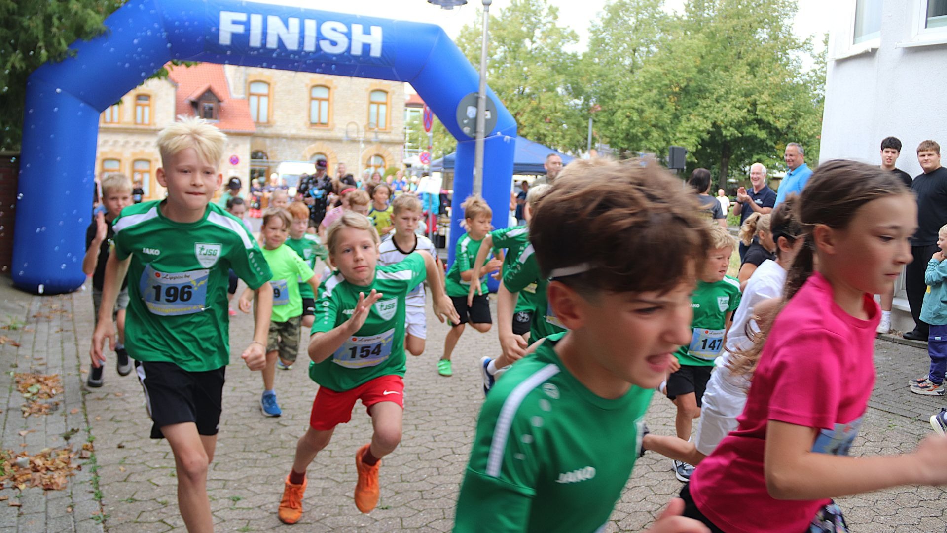 Kinder rennen unter einem blauen Zielbogen mit der Aufschrift „FINISH“ auf einer gepflasterten Straße