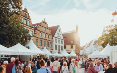 Viele Menschen schlendern zwischen weißen Verkaufsständen auf einem belebten Weinmarkt in einer Altstadt bei