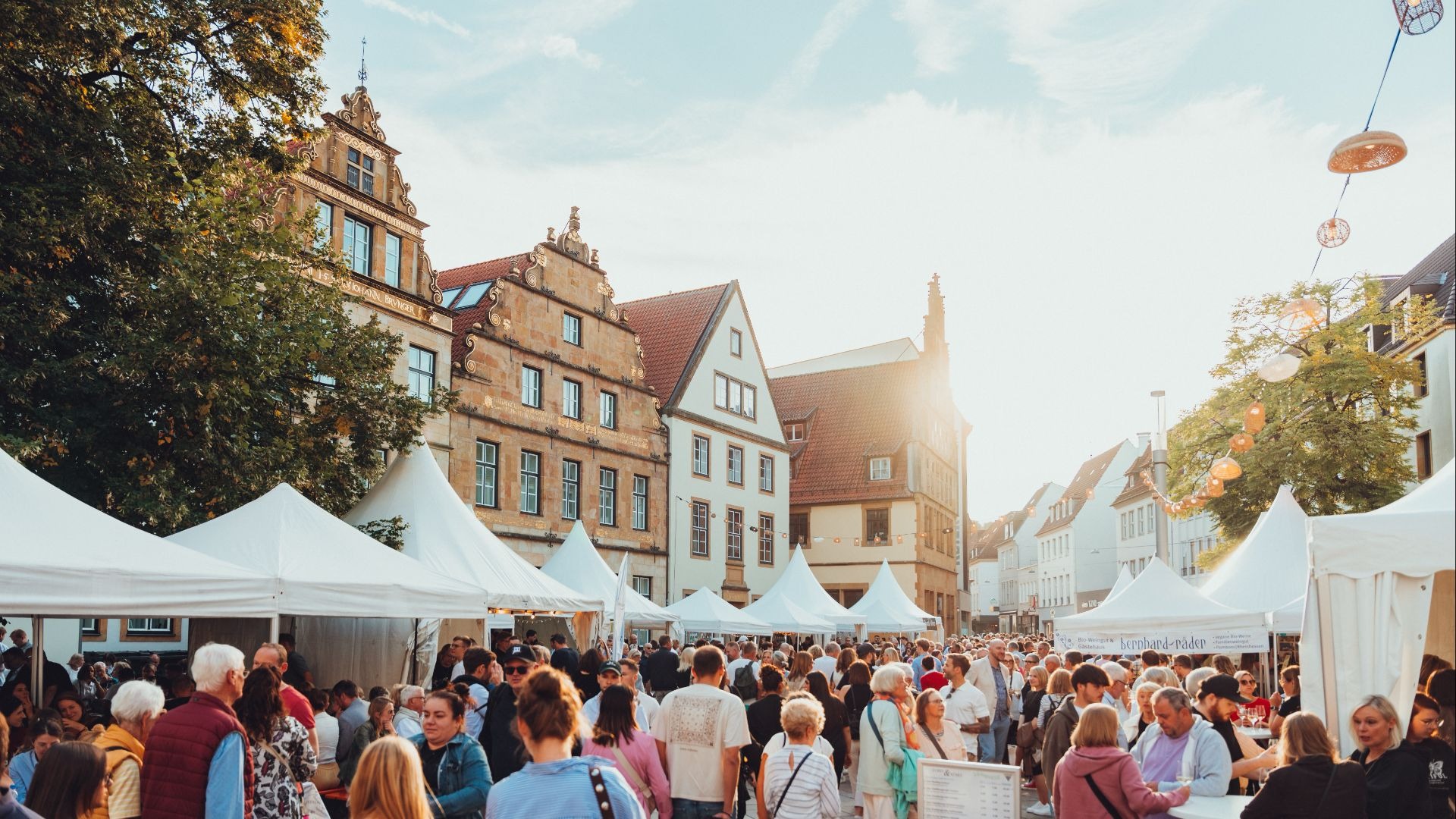 Viele Menschen schlendern zwischen weißen Verkaufsständen auf einem belebten Weinmarkt in einer Altstadt bei