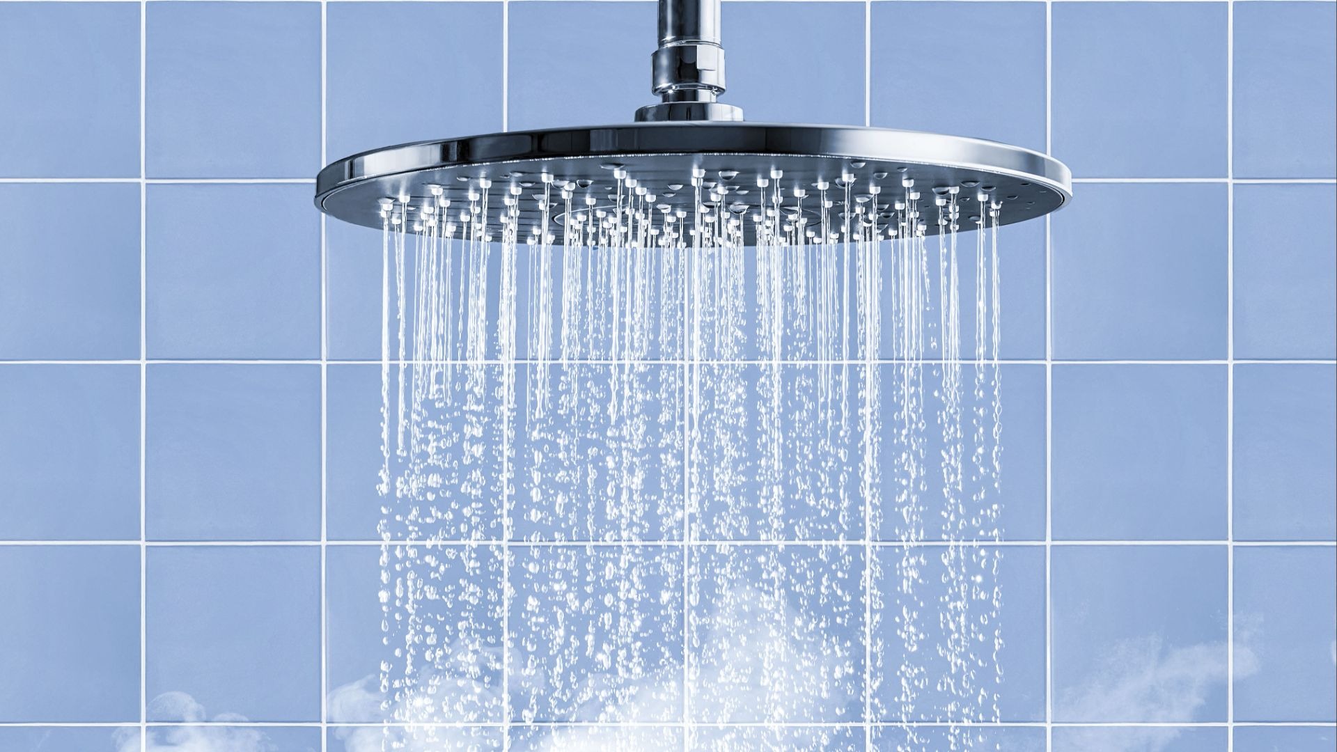 Ein Duschkopf sprüht Wasserstrahlen vor blauen Fliesen und aufsteigendem Dampf