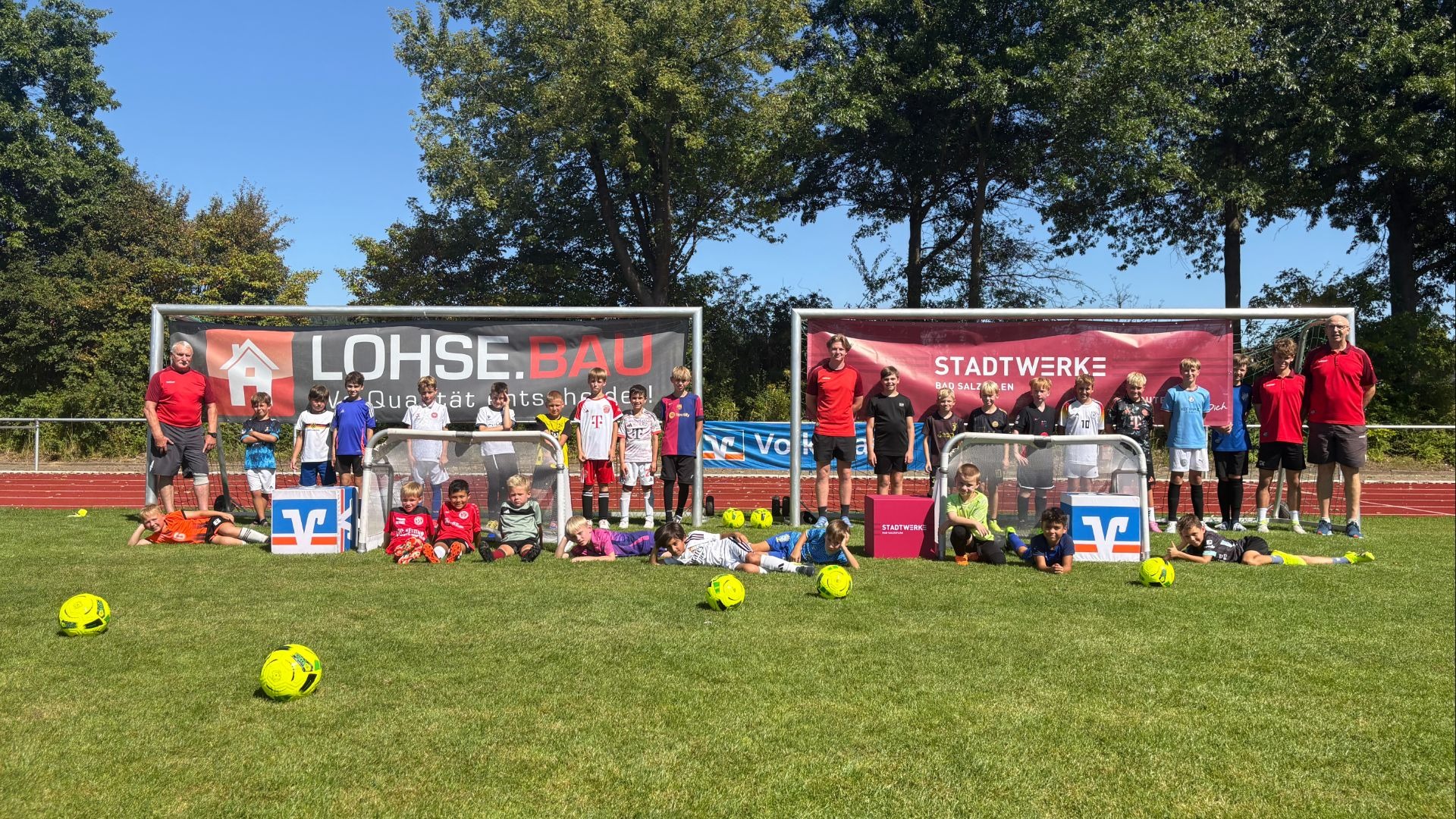 Gruppe Kinder und Erwachsene auf Fußballfeld beim Bad Salzufler Camp, teils liegend, mit Toren und Bällen