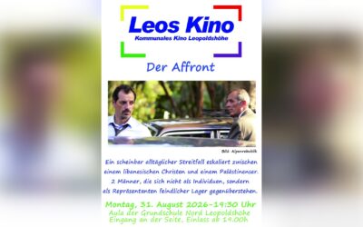 Zwei Männer mit ernsten Gesichtern stehen sich im Freien gegenüber, zwischen ihnen ist ein Auto erkennbar